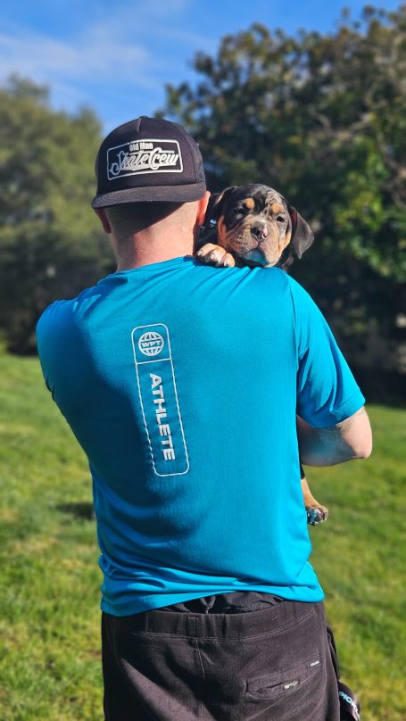 Person in a blue shirt holding a small dog outdoors.